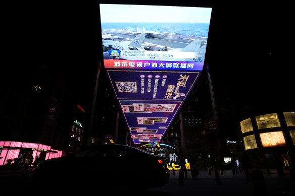 An evening news broadcast shows Chinese fighter jets on an aircraft carrier around Taiwan on an outdoor screen in Beijing.