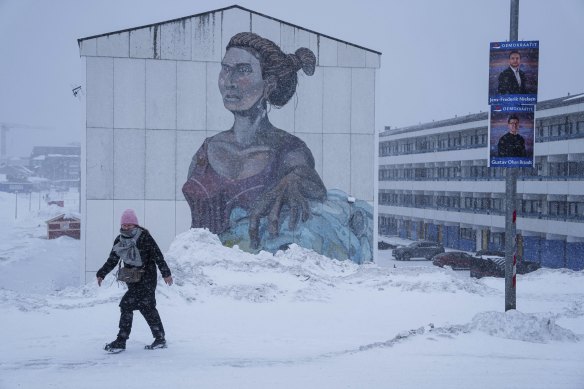 A woman walks on a street with posters for the upcoming elections in Nuuk, Greenland.