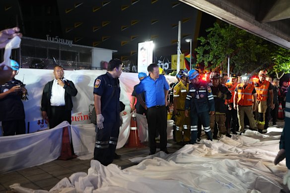 Il primo ministro thailandese Anutin Charnvirakul, in blu, ispeziona il luogo di un incendio mentre i corpi delle vittime vengono deposti lunedì in fila a Bangkok