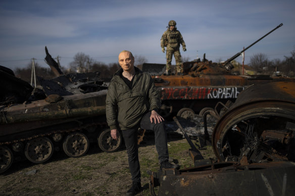 A man wearing a Vladimir Putin mask  poses for a picture in front of the ruins of a Russian tank near Bucha. 
