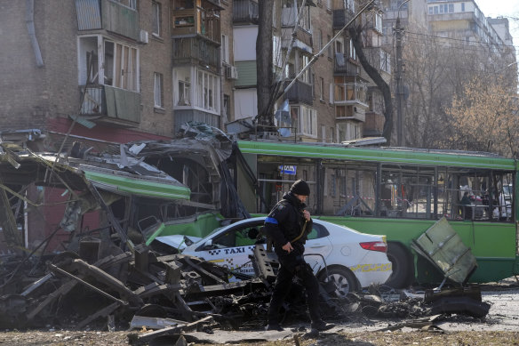 A Ukrainian soldier walks by a destroyed bus and taxi in the city of Kyiv.