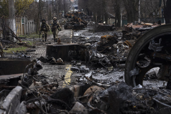 Askerler, Nisan 2022'de Kiev'in eteklerindeki Bucha'da imha edilmiş Rus tanklarının arasında yürüyor.