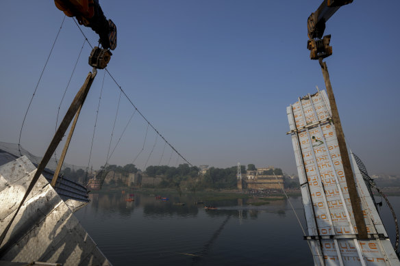 Workers use machinery to remove the debris of a pedestrian bridge that collapsed in Morbi. 