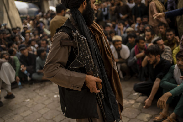 A Taliban fighter controls a crowd waiting to withdraw money from a bank. 