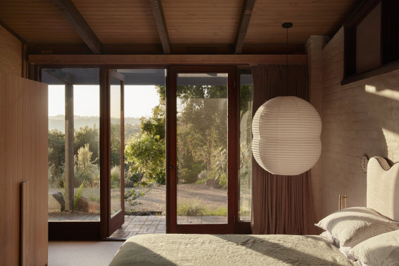 In the main bedroom, floor-to-ceiling windows connect to the landscape while the bagged brick wall frames an over-scale paper lantern.