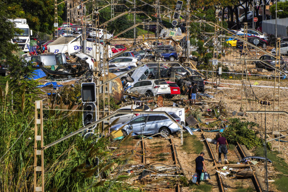 People walk among flooded cars piled up in Valencia, Spain.
