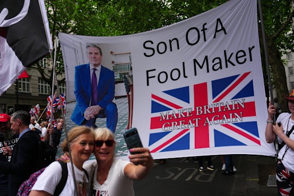 Pessoas posam para uma foto em frente a um banner visando o primeiro-ministro do Reino Unido, Keir Starmer.
