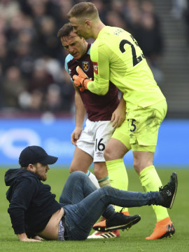 A pitch invader falls to the pitch confronted by West Ham's Mark Noble, with goalkeeper Joe Hart, right.