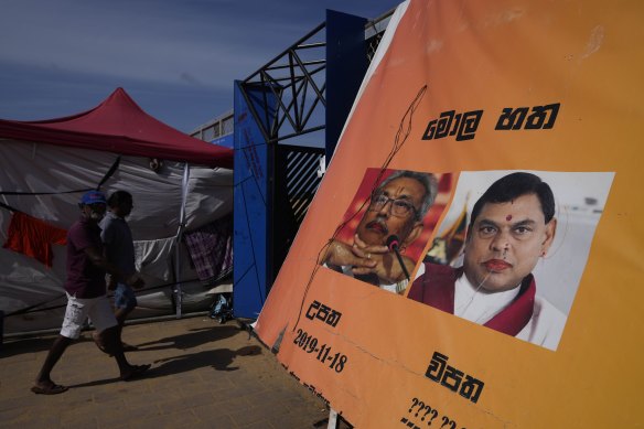 People walk past a poster showing defaced portraits of president Gotabaya Rajapaksa and his brother Basil.