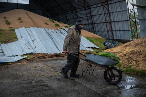 A worker shovels grain into a wheelbarrow after it was ruined when a storage barn was damaged during fighting on October 23, in Izyum, Kharkiv.