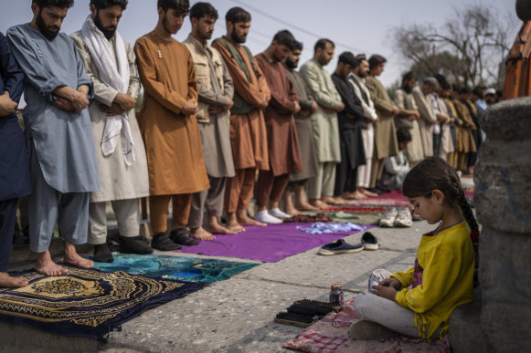 An Afghan girl working as a shoe cleaner sits in the street while men pray during Friday prayers in Kabul, Afghanistan, last week.