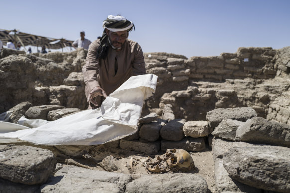 A worker covers skeletal remains found at the site of a 3000-year-old lost city in Luxor, Egypt. 