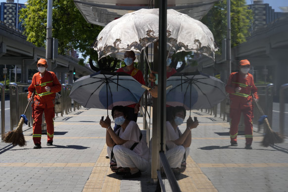 People shelter from the sun under umbrellas as they wait for a bus in Beijing.