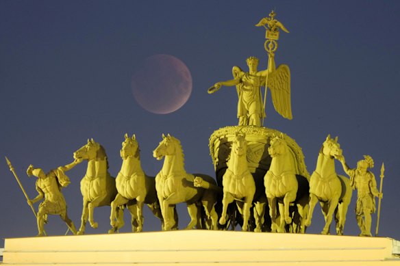 The full moon rises behind a sculpture of a chariot at the Palace Square for a total lunar eclipse in St. Petersburg, Russia.