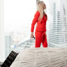 Stewardess in red uniform arrives in a hotel room with black suitcase. Rest in the transit city before the return flight. Young blond Woman in red coral suit iStock image for Traveller. Re-use permitted.