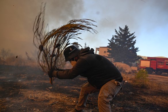 A volunteer tries to extinguish small flames northwest of Athens.