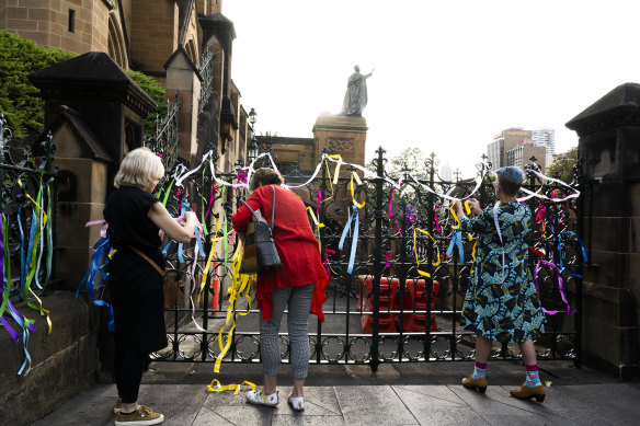 Victim-survivors and supporters tie ribbons earlier this morning.