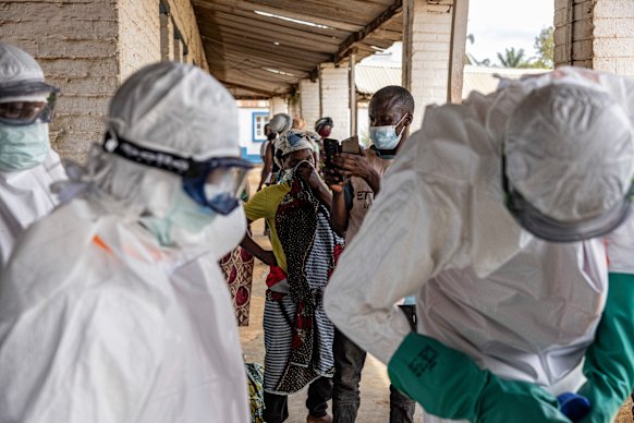 Health workers wearing protective suits prepare for Ebola response operations as residents gather outside a hospital in Mongbwalu, Democratic Republic of the Congo.