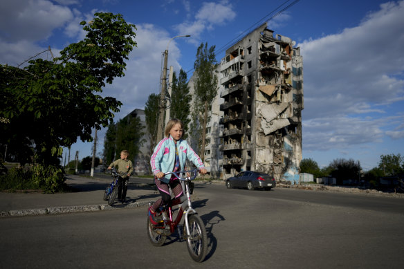 A girl rides a bicycle in front of houses ruined by shelling in Borodyanka.