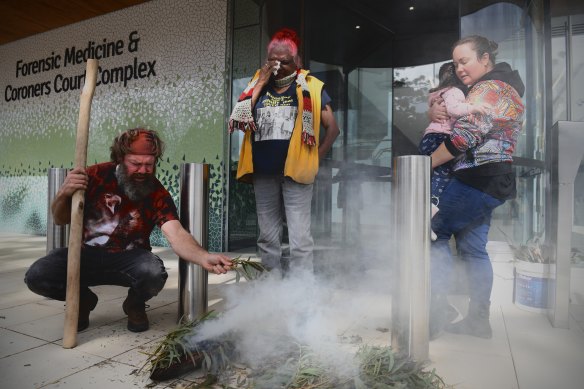Locky Magic Dennis (left), Ruby Dykes wiping her eyes (centre) and Fleur Magic Dennis during a smoking ceremony in memory of Mootijah outside the Coroners Court in Sydney.


