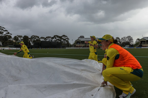 Australian players assist the ground staff amid the threatening clouds.