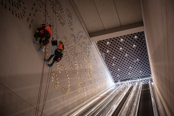 Workers abseil a wall to assemble a giant artwork of 1000 Indigenous footprints.