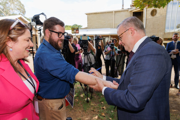 Anthony Albanese writes and signs a “No Change To WA GST” pledge on the arm of West Australian reporter Dylan Caporn in February 2024.