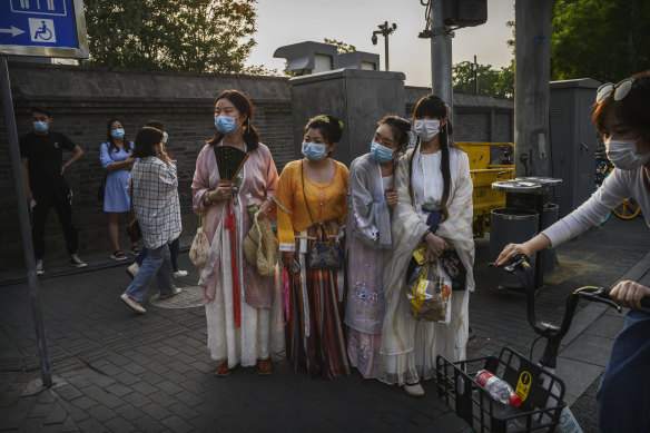 Chinese women wear traditional clothing and protective masks as they wait to cross a road in a tourist area during the May holiday in Beijing.