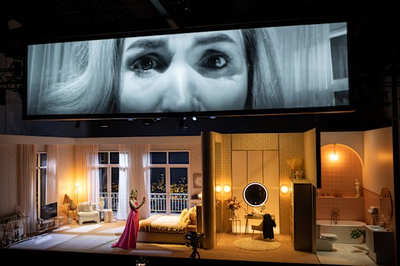 The set is a hotel room with a video screen above.