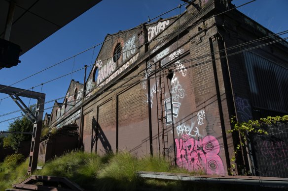 The old Newtown tram sheds, next to Newtown railway station, are tagged with graffiti and overgrown with vegetation.