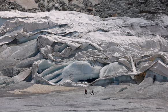 Alpinists hiking on the receding Rhone glacier walk past a portion at the very bottom of the glacier that is covered in reflective tarp on June 20, 2022.