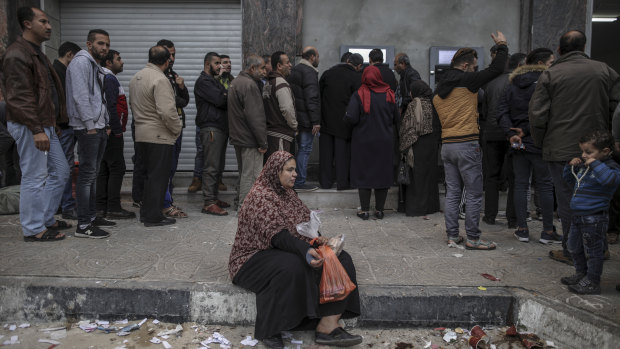 A woman begs for money as residents of Gaza line up to withdraw what money they can from ATMs