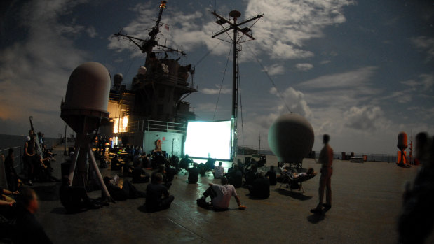 Sailors assigned to amphibious command ship USS Blue Ridge watch a movie on the ship's main deck.