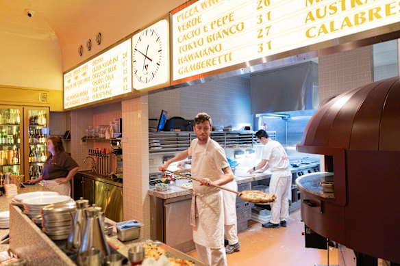 The pizzeria is bathed in a yellow light, punctuated by neon signage.