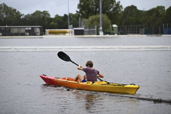 A boy kayaks over a flooded cricket oval in Tingalpa on Brisbane’s Eastside.