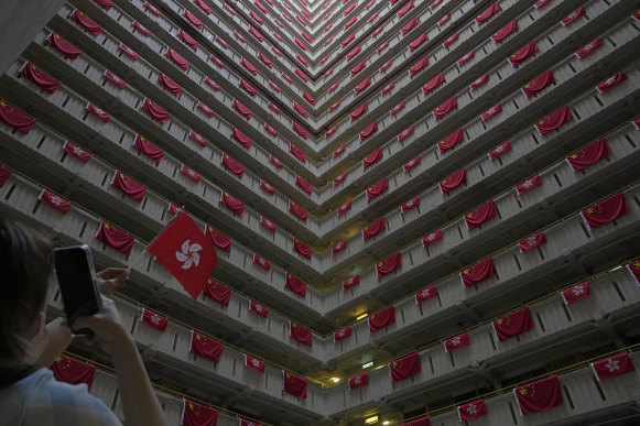 A woman takes a photo of the Chinese and Hong Kong flags hanging from a housing estate to celebrate the 25th anniversary of Hong Kong handover to China.