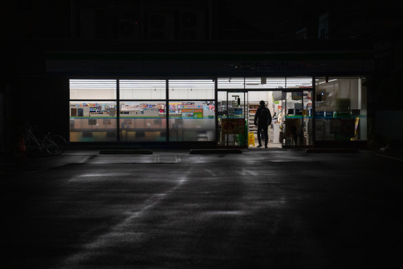 A man enters a convenience store that has turned off its exterior lighting to conserve energy in Tokyo, Japan. 