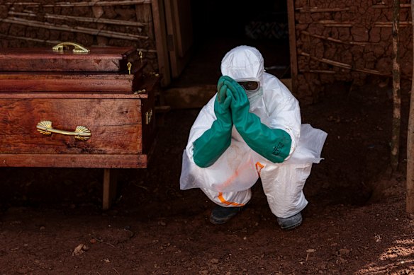 A health worker crouches beside the coffin of a suspected Ebola victim during safe burial procedures outside a family home in Mongbwalu last month.