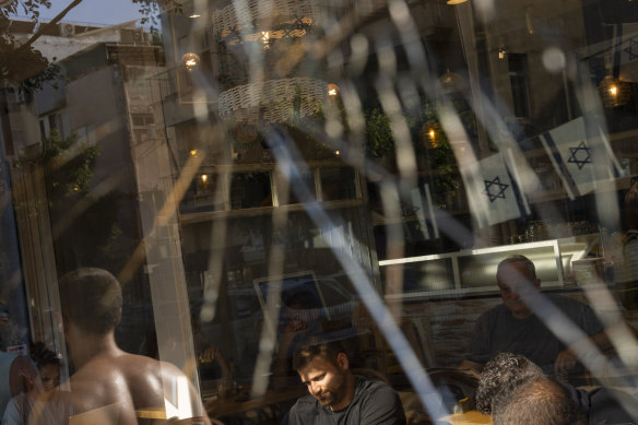 People are seen through a broken coffee shop window next to the scene of an explosive drone attack in Tel Aviv.