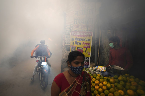 Commuters walk past smoke from fumigation in a densely populated area in New Delhi, India, Wednesday, October 27, 2021.