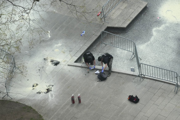 New York Police officers inspect a backpack left at the scene where a man lit himself on fire in a park outside Manhattan criminal court, Friday, April 19, 2024