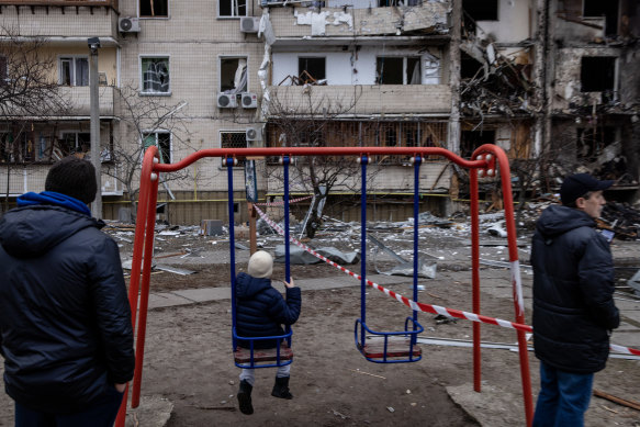 A boy plays on a swing in front of a damaged residential block hit by an early morning missile strike on February 25, 2022.