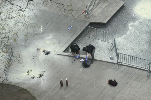 New York Police officers inspect a backpack left at the scene where a man lit himself on fire in a park outside Manhattan criminal court.