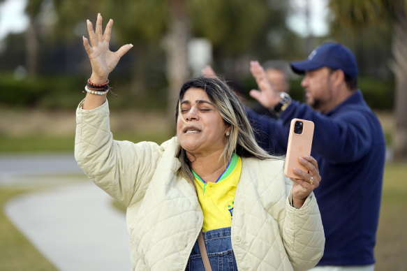 A woman leads a group of supporters of former Brazilian president Jair Bolsonaro in a prayer , on Friday outside the Florida house where he is staying. Supporters received autographs by Bolsonaro, but he did not come out to see them.