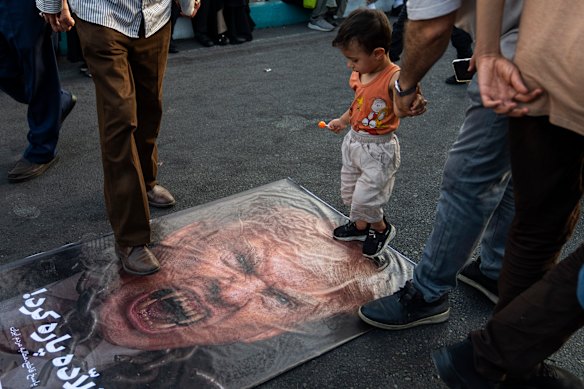  Iranian protesters and a child step on a poster with a vampire-like illustration of US President Donald Trump in Revolution Square to protest against US attacks on nuclear sites in Iran