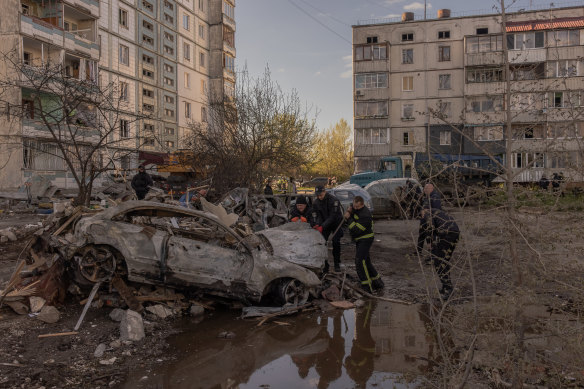 Policemen and emergency personnel check a burned car at the site of the destroyed residential building that was hit during the Russian attack on Uman.