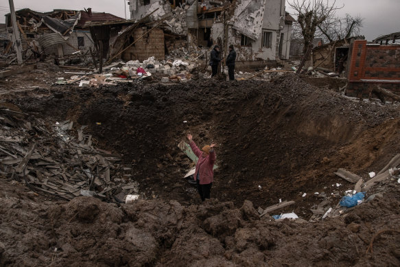 A woman waves as she stands in a crater following the Russian missile attacks on January 26 in Kyiv.