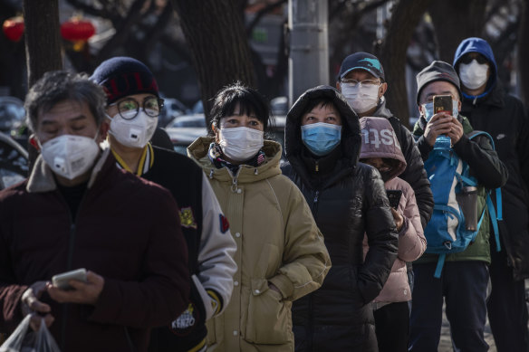 Chinese customers wear protective masks as they line up single file to buy dumplings at a popular local shop in Beijing, China. Due to the world's reliance on Chinese goods, the impacts of the coronavirus could spread far.