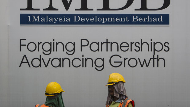 Construction workers chat in front of a billboard for state investment fund 1 Malaysia Development Berhad (1MDB) at the fund's flagship Tun Razak Exchange development in Kuala Lumpur, Malaysia.