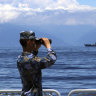 A People’s Liberation Army member watches military exercises, with Taiwan’s frigate Lan Yang in the background.